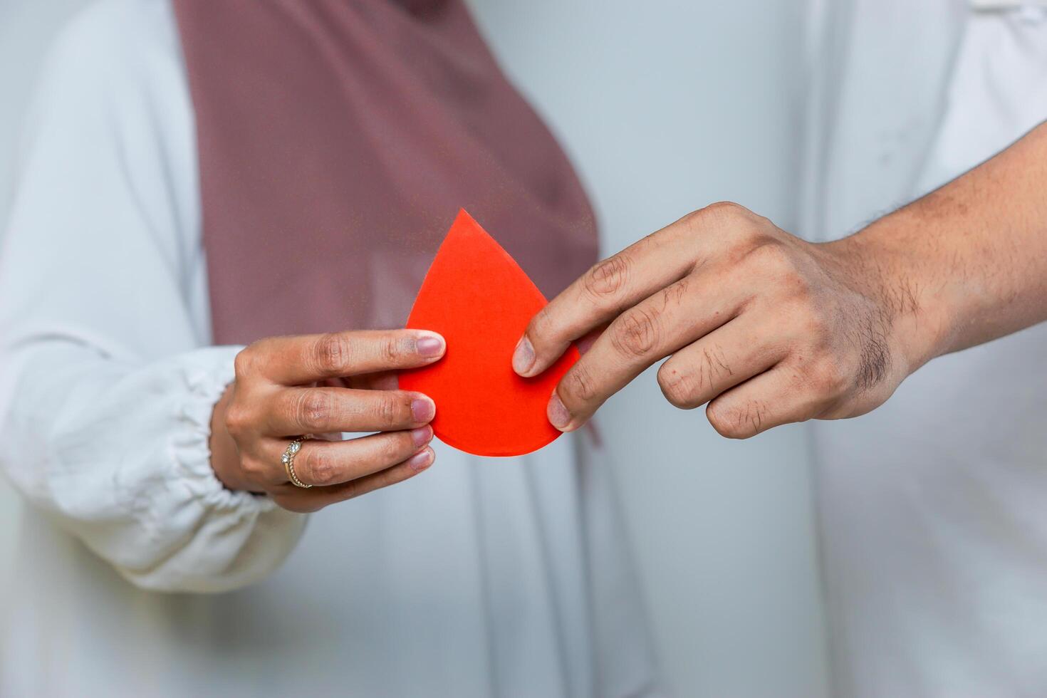 Two hands holding a red paper drop together, symbolizing blood donation and teamwork for a cause. blood donor day photo