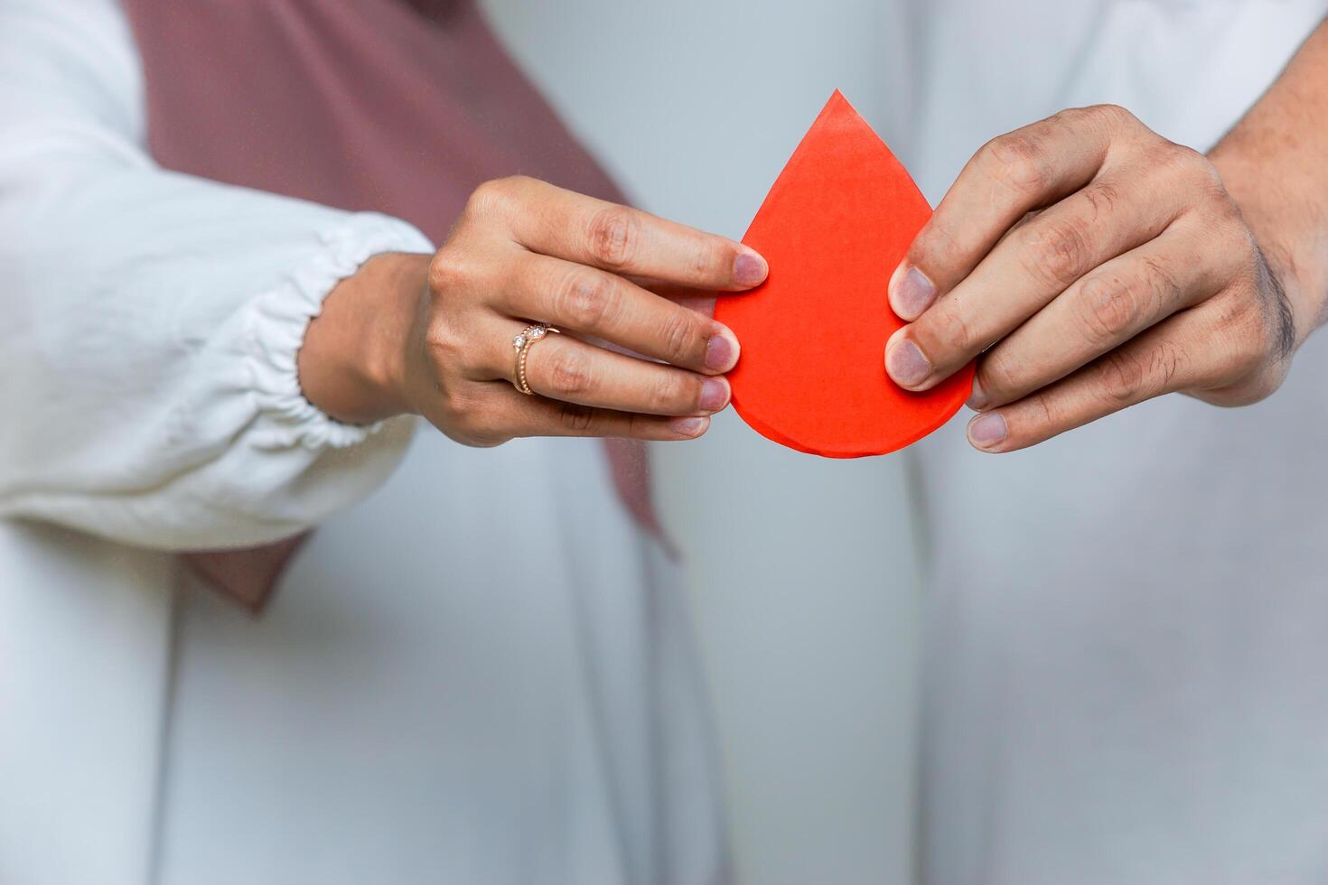 Two hands holding a red paper drop together, symbolizing blood donation and teamwork for a cause. blood donor day photo