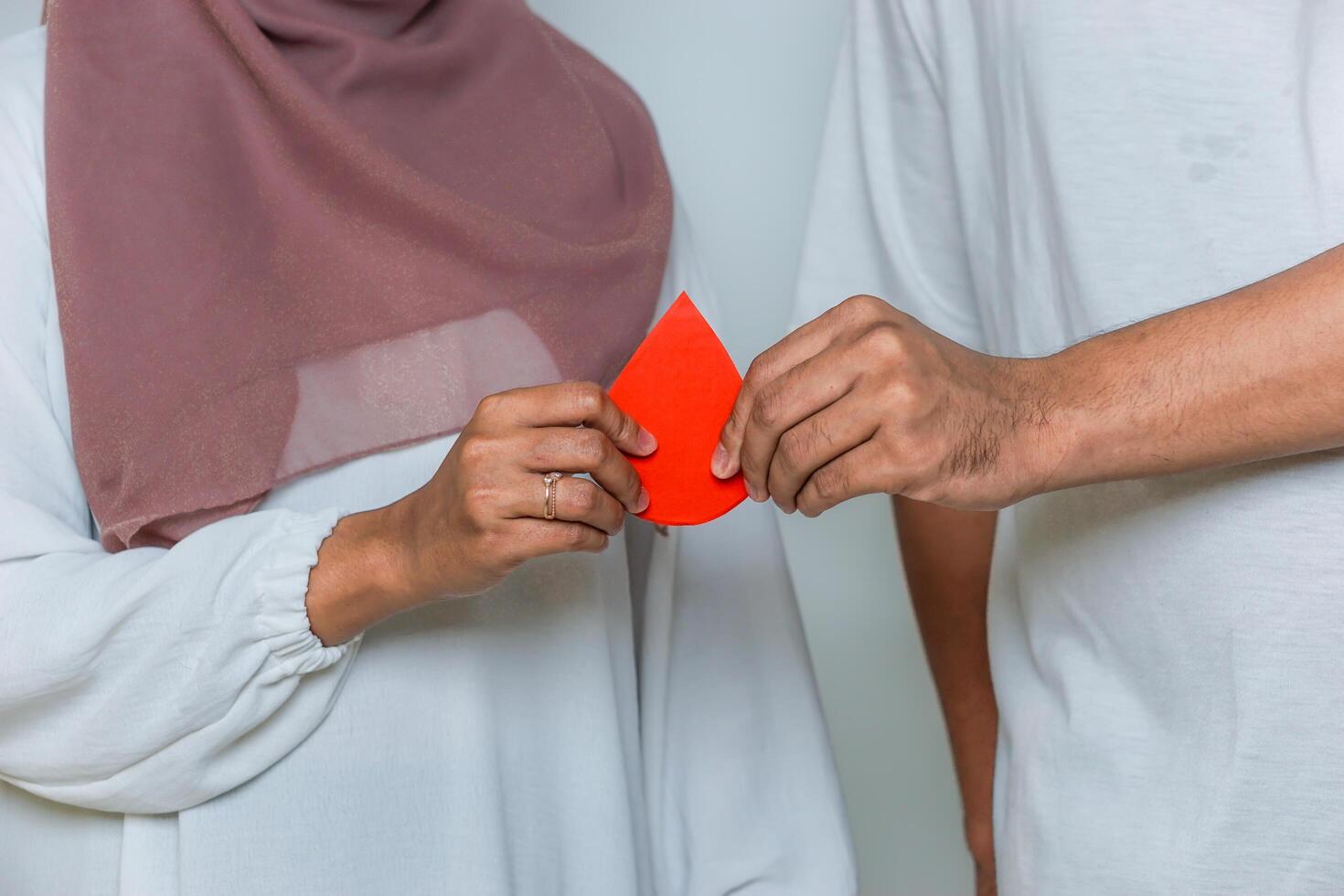 Two hands holding a red paper drop together, symbolizing blood donation and teamwork for a cause. blood donor day photo