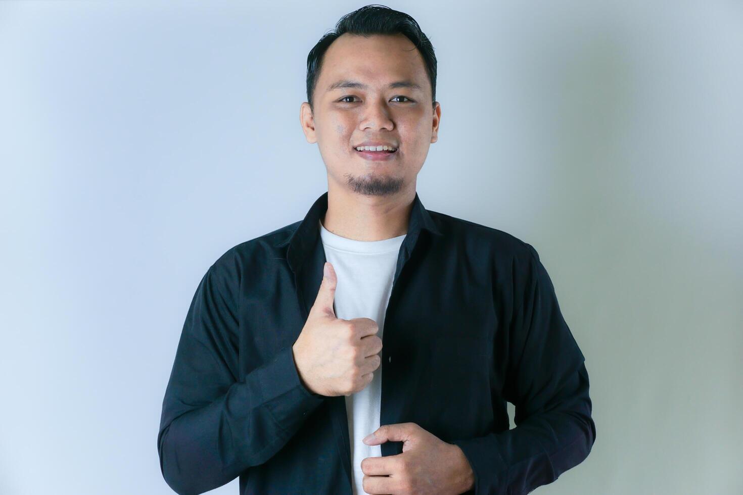 A man in a black shirt gives a thumbs-up, exuding confidence and positivity against a clean white background. photo