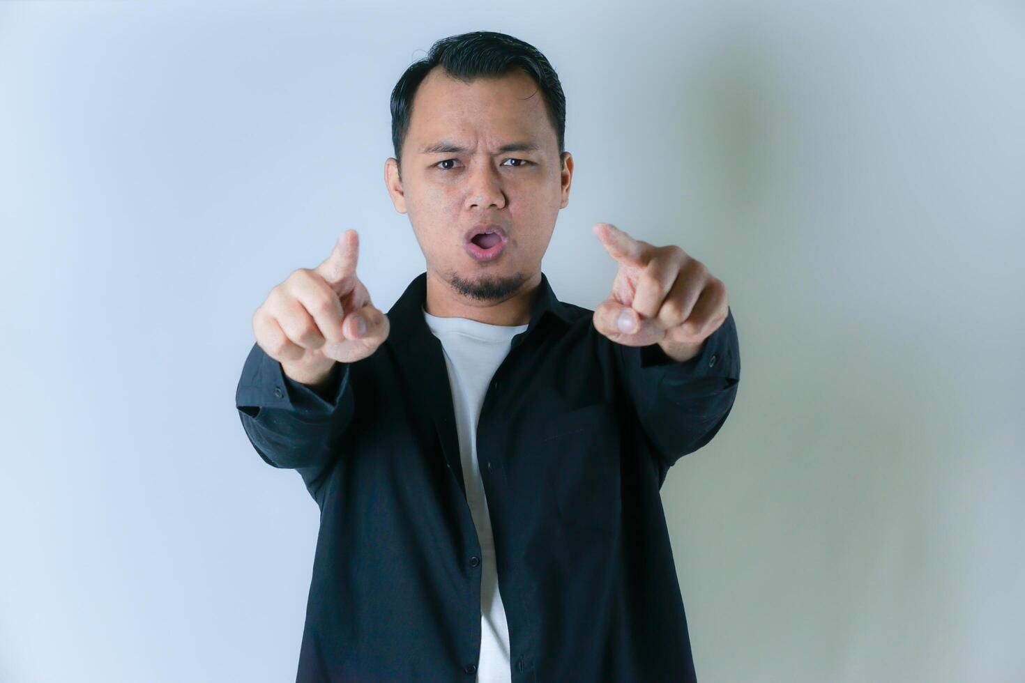 A man in a black shirt points both index fingers at the camera against a plain background, conveying a strong and assertive expression. photo