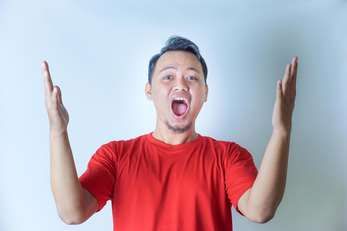 A man in a red shirt joyfully raises his fists in a celebratory gesture, smiling widely against a plain white background. photo