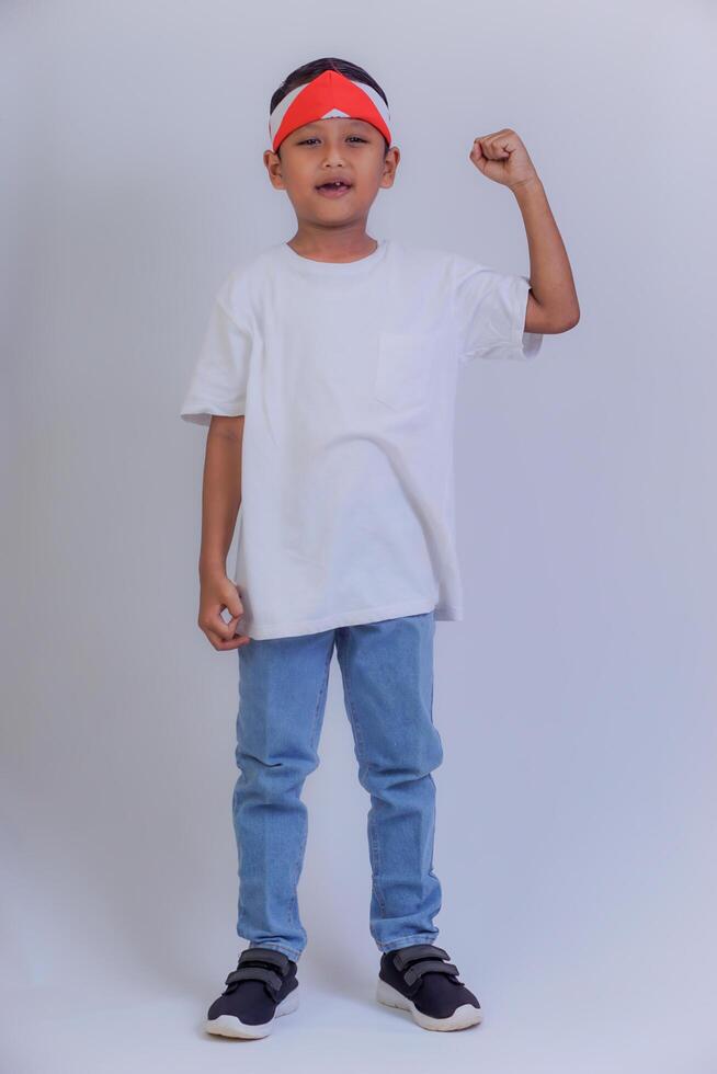 A young boy wearing a red headband, white t-shirt, and blue jeans, making a power pose with his fist. photo