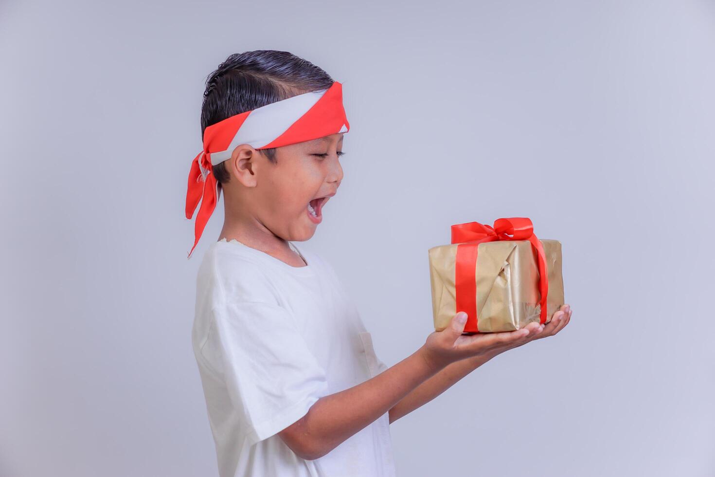 A joyful child wearing a headband, smiling widely while holding a gift wrapped with red ribbon. photo