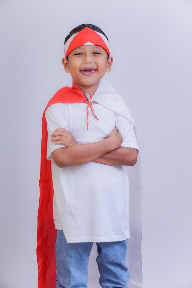A boy in a red and white costume smiles confidently with a headband and Indonesian flag on his back photo