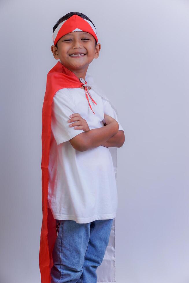 A boy in a red and white costume smiles confidently with a headband and Indonesian flag on his back photo