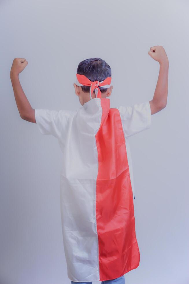 A child wearing a red-and-white robe, raising a fist, shows pride and enthusiasm. photo