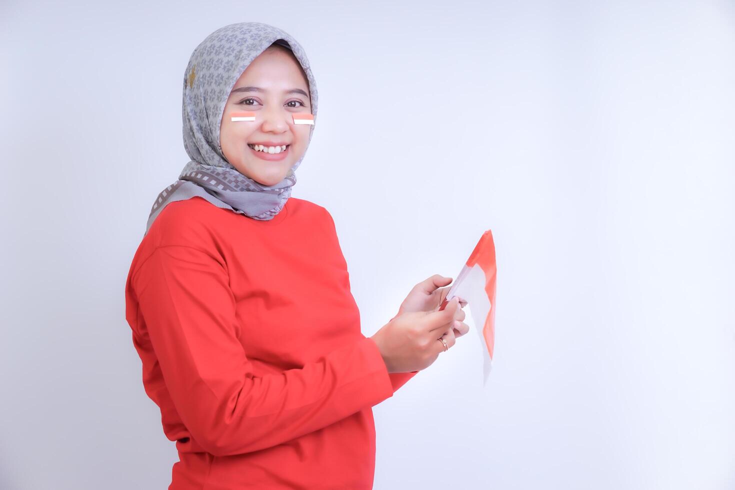 A woman in a red shirt, smiling and holding phone and Indonesian flag. Concept of celebrating Indonesia Independence Day. photo