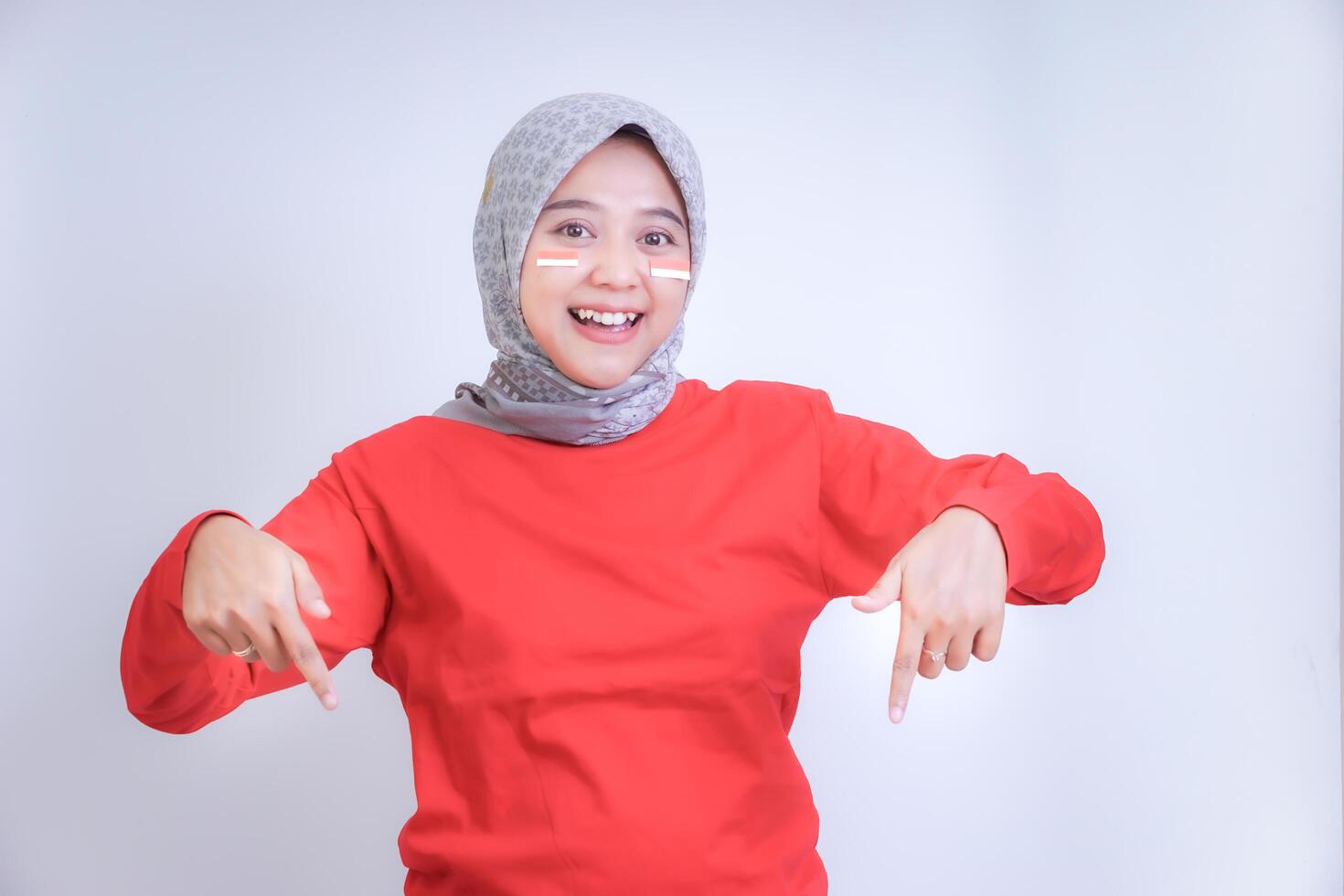 A woman in a red shirt smiles and points downward with both hands. Concept of celebrating Indonesia Independence Day. photo