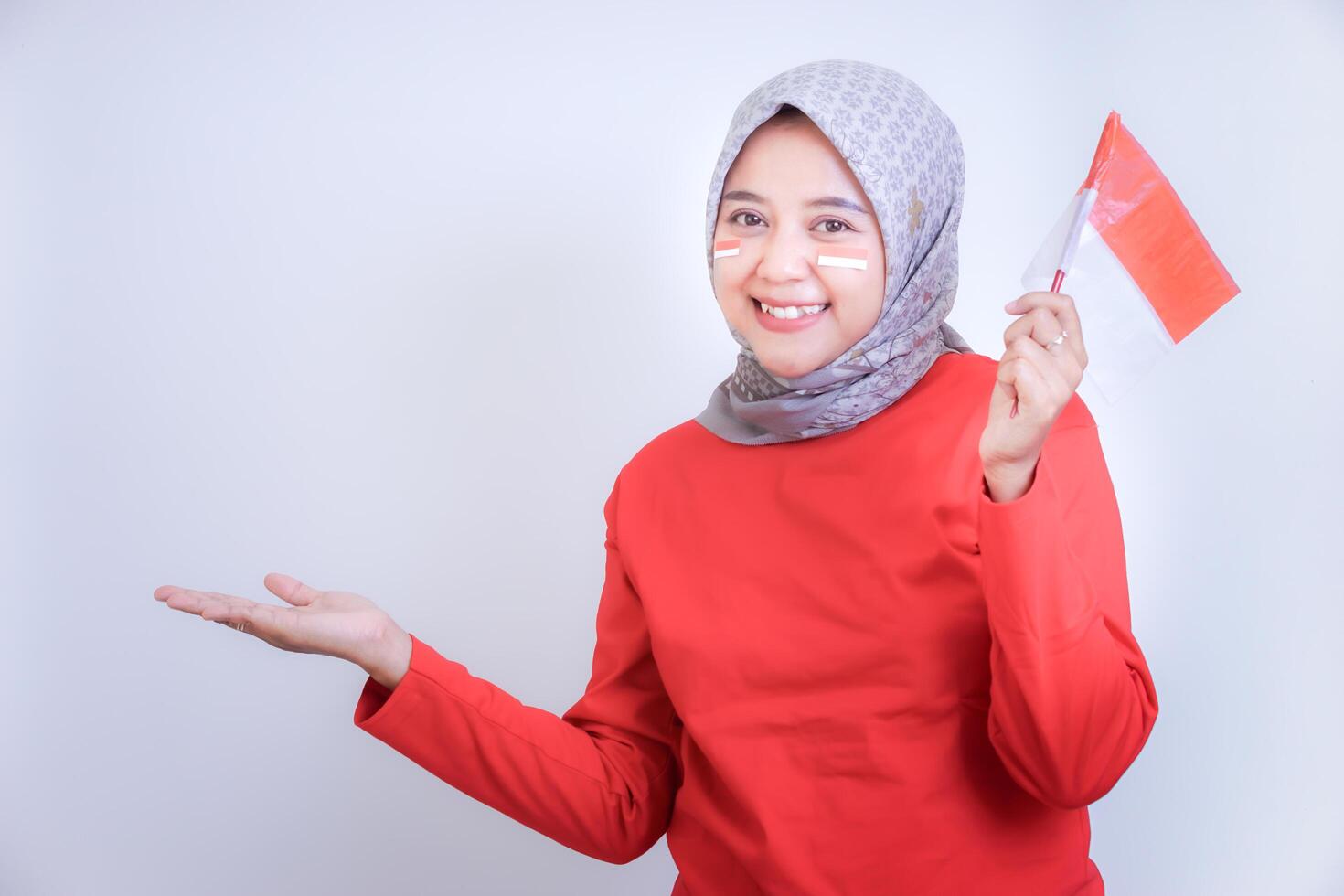 A happy woman in a red outfit holds the Indonesian flag, smiling excitedly. Concept of celebrating Indonesia Independence Day. photo