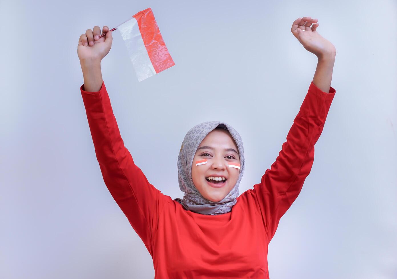 A cheerful woman in a red dress holding the Indonesian flag with a big smile. Concept of celebrating Indonesia Independence Day. photo