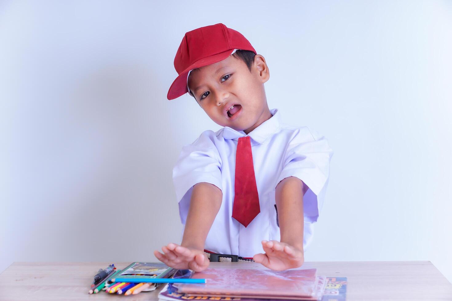 An Indonesian boy in school uniform points to a book on a table with an expression of refusal to learn photo
