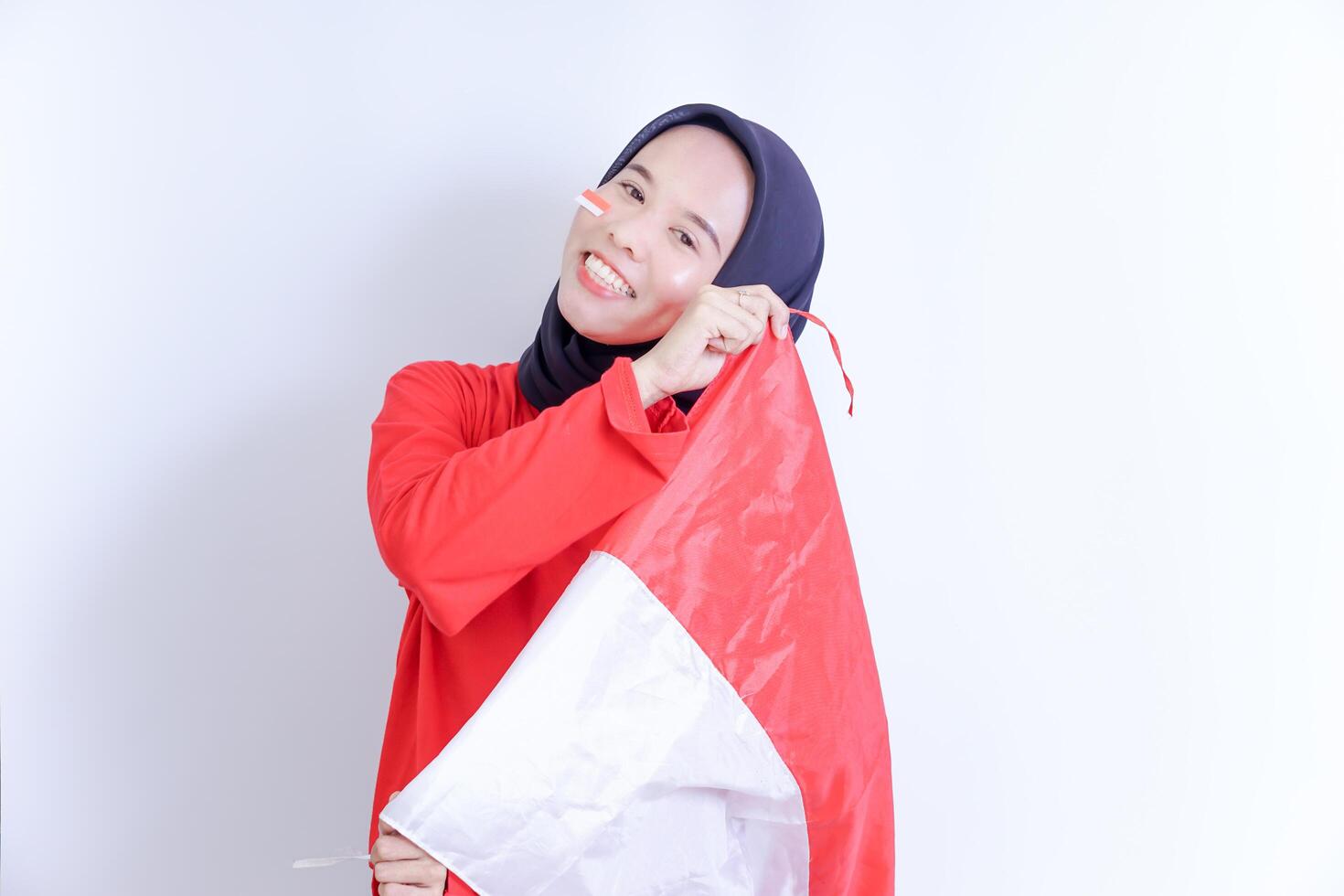 A young Indonesian woman wearing a hijab, with a big smile on her face, holds a red and white flag in her hands. celebrating Indonesia's independence day on August 17th photo