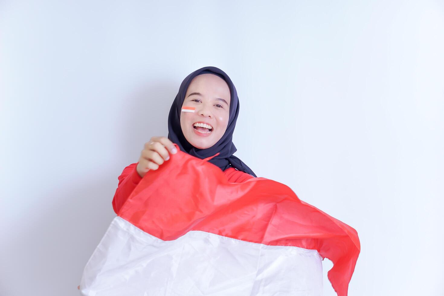 A young Indonesian woman wearing a hijab, with a big smile on her face, holds a red and white flag in her hands. celebrating Indonesia's independence day on August 17th photo