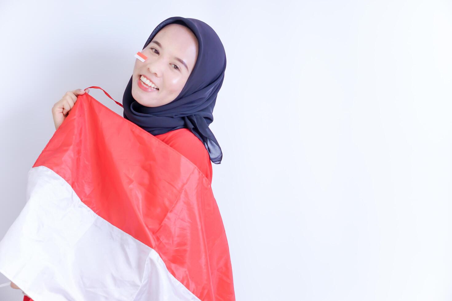 A Indonesian young woman wearing hijab is smiling brightly as she holds up a red and white flag, expressing her patriotism and joy to celebrate Indonesian independence day on 17 August. photo
