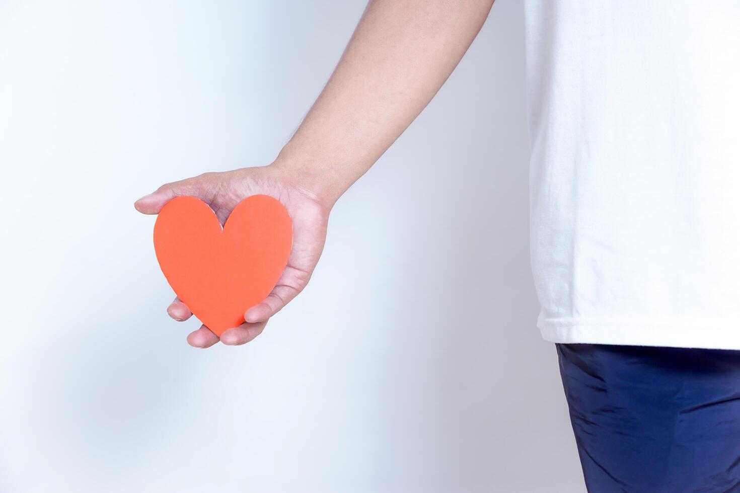 A hand holds a vibrant red heart, symbolizing love and affection against a clean, white background. World Heart Day concept photo