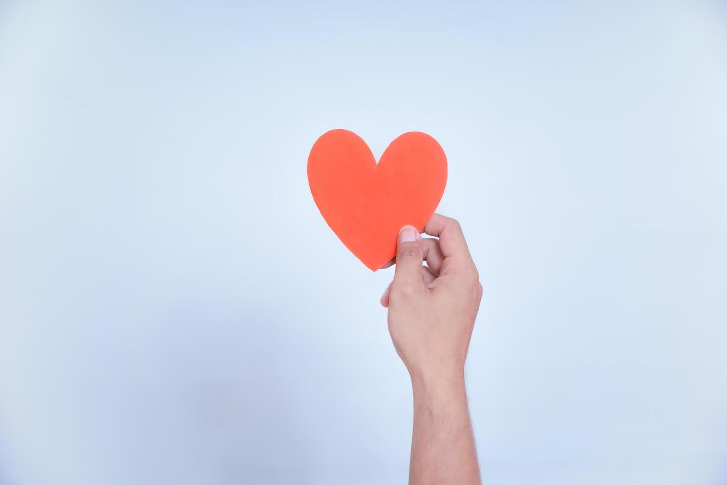 A hand holds a vibrant red heart, symbolizing love and affection against a clean, white background. World Heart Day concept photo