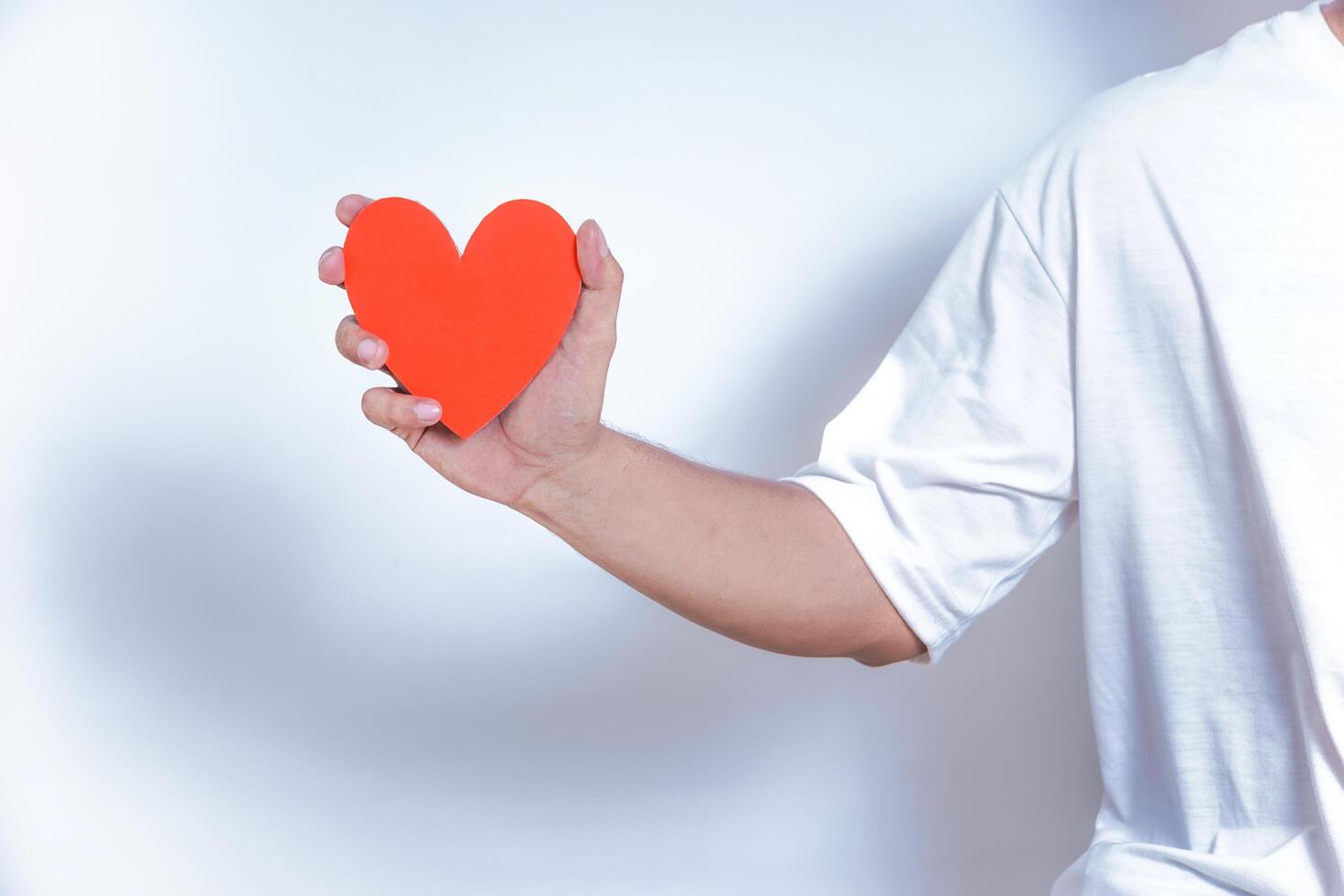 A hand holds a vibrant red heart, symbolizing love and affection against a clean, white background. World Heart Day concept photo