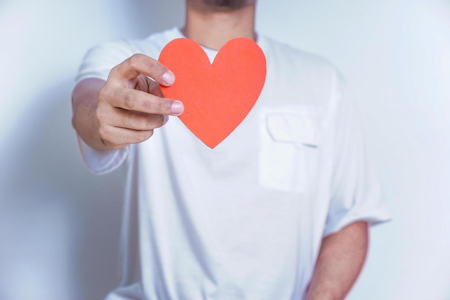 A person holds up a red heart-shaped cutout, symbolizing love and affection against a clean white background. World Heart Day concept photo