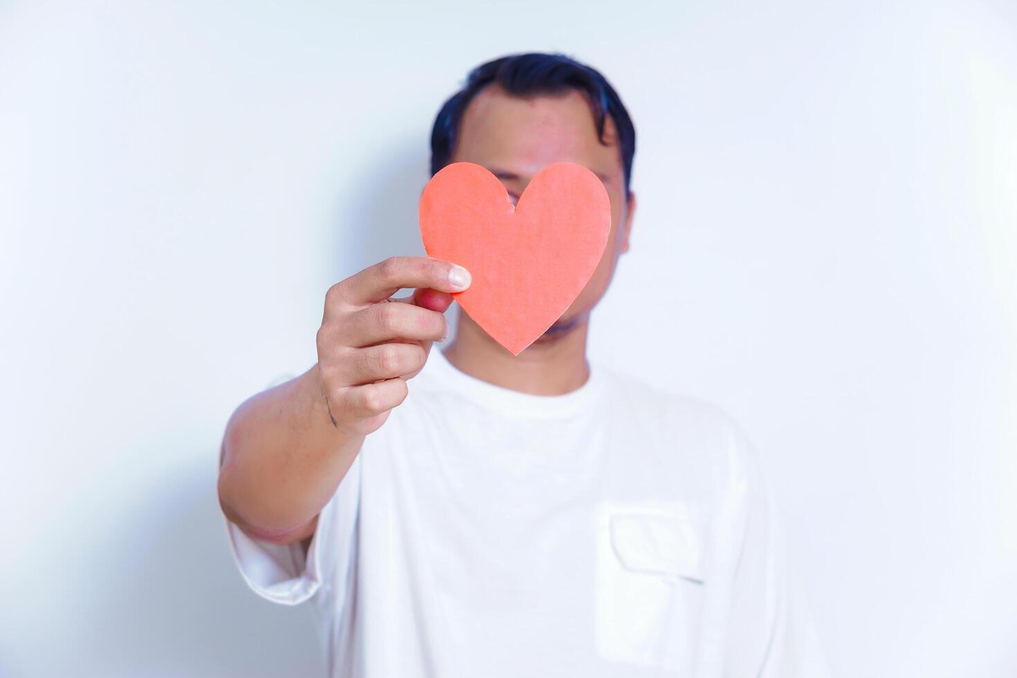 A person holds up a red heart-shaped cutout, symbolizing love and affection against a clean white background. World Heart Day concept photo