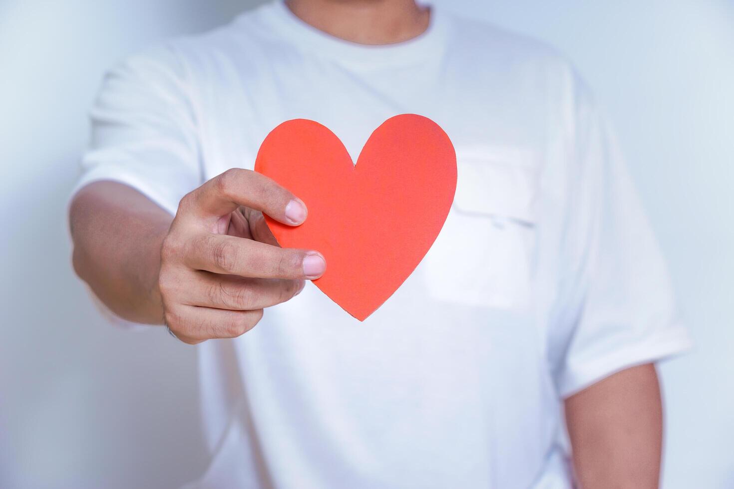 A person holds up a red heart-shaped cutout, symbolizing love and affection against a clean white background. World Heart Day concept photo