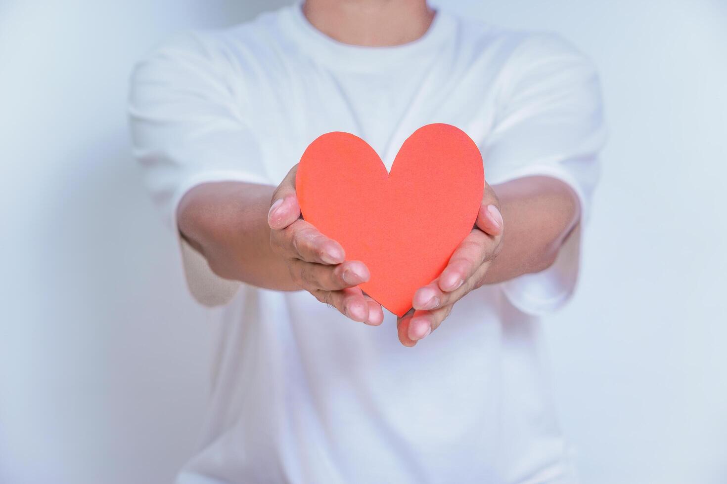 A person holds up a red heart-shaped cutout, symbolizing love and affection against a clean white background. World Heart Day concept photo