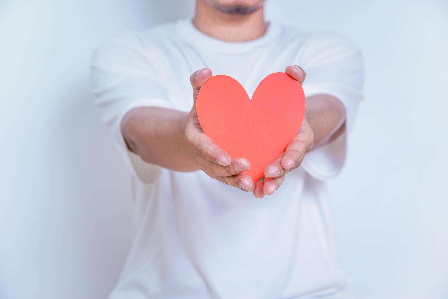 A person holds up a red heart-shaped cutout, symbolizing love and affection against a clean white background. World Heart Day concept photo