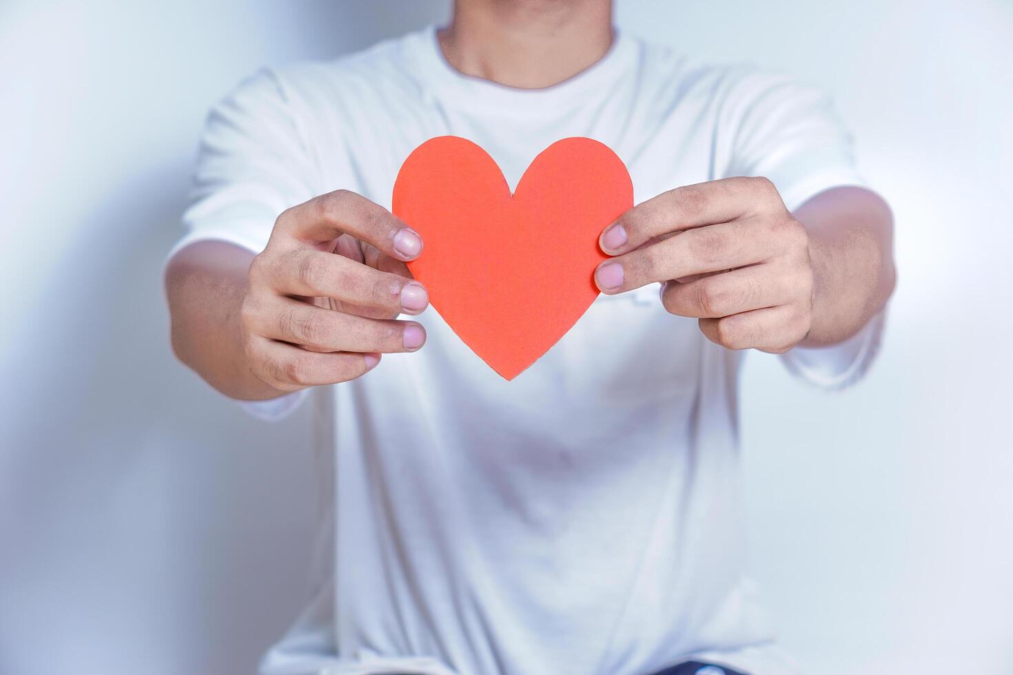 A person holds up a red heart-shaped cutout, symbolizing love and affection against a clean white background. World Heart Day concept photo