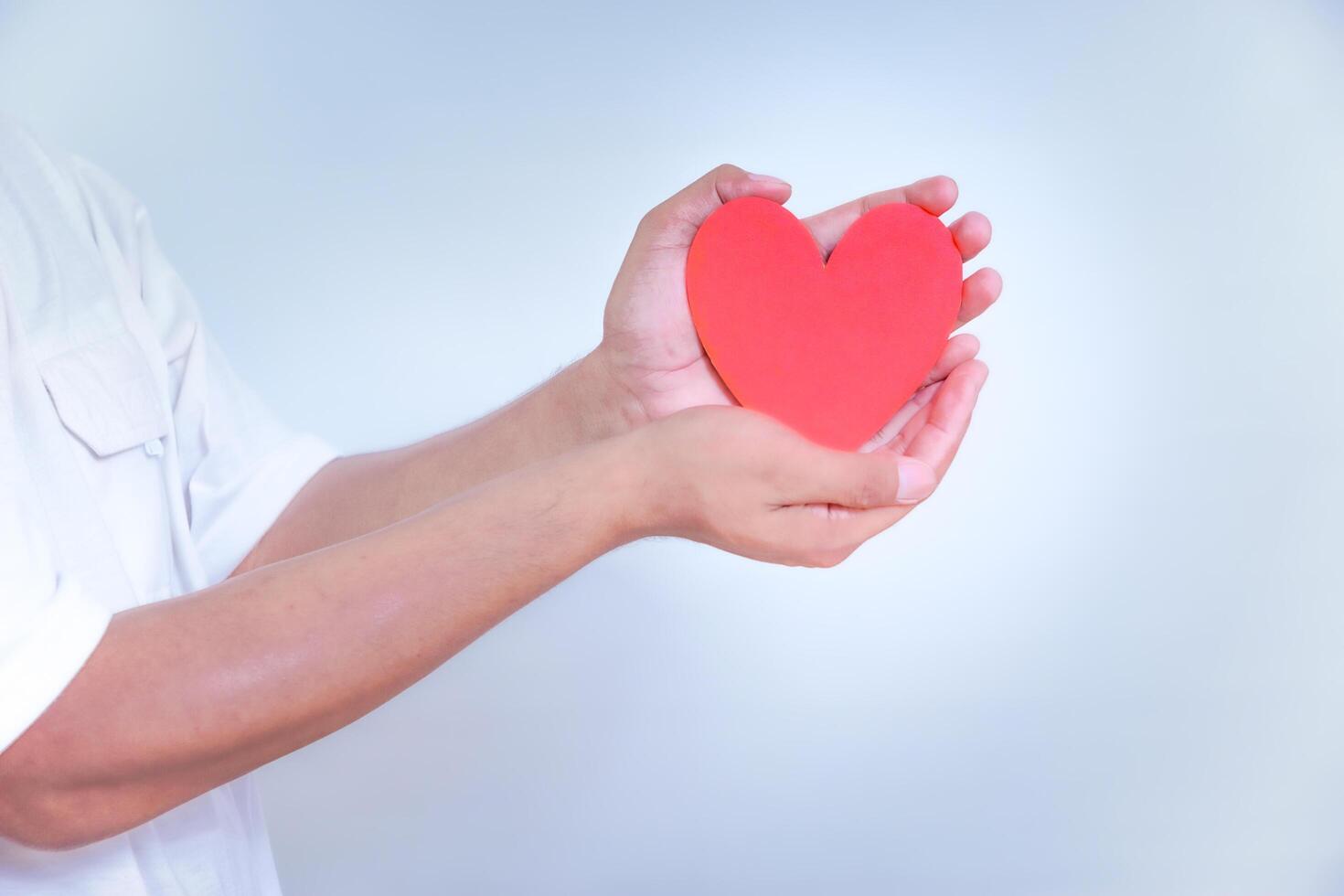 A hand holds a vibrant red heart, symbolizing love and affection against a clean, white background. World Heart Day concept photo