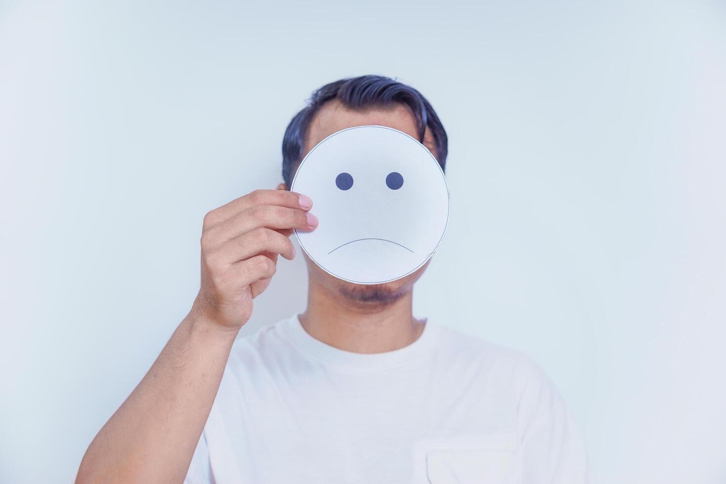 A person holds a sad face symbol, reflecting emotions and the complexity of feelings we often hide. world mental health day concept photo