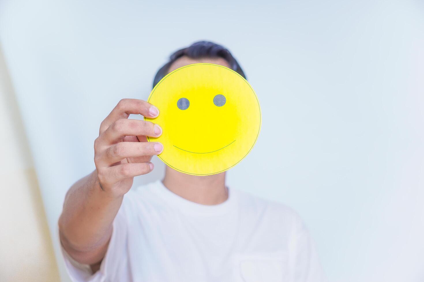 A person holding a cheerful yellow smiley face symbolizes joy and positivity in a bright setting. world mental health day concept photo