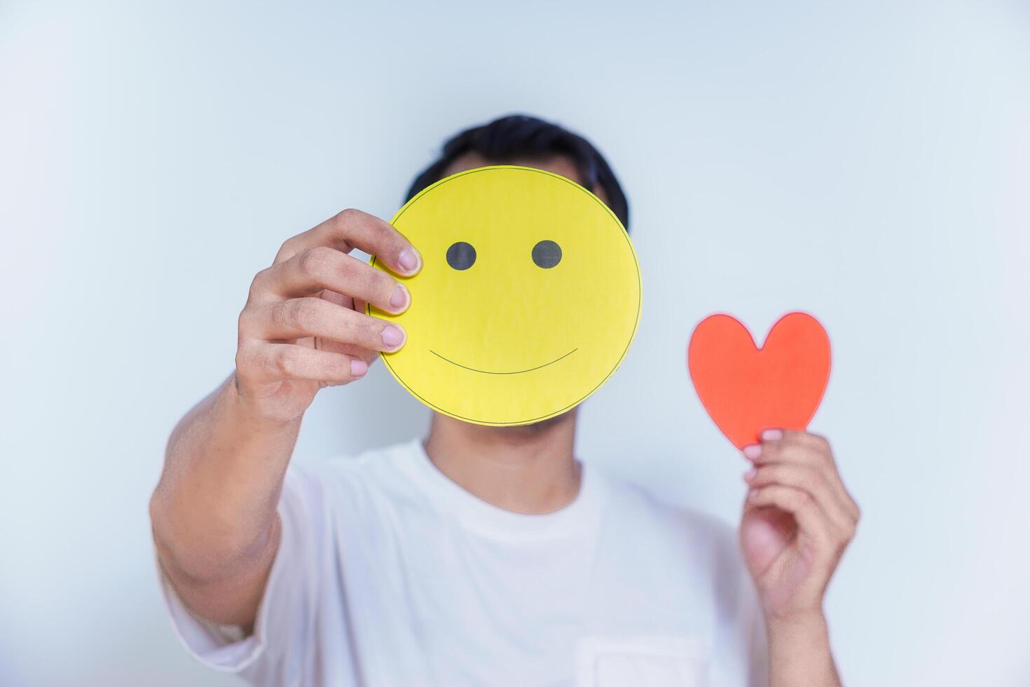A person holds a smiling face and a heart, symbolizing happiness and love in a simple yet expressive way. world mental health day concept photo