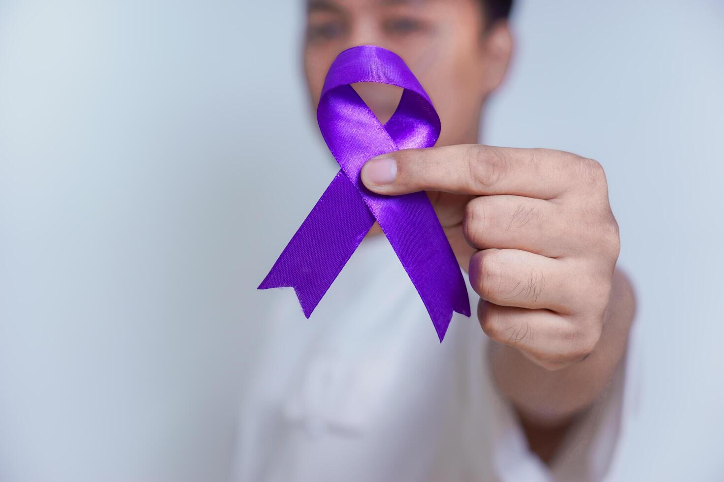 A person holding a purple ribbon, symbolizing awareness and support for various causes, including cancer. Healthcare and World cancer day concept photo