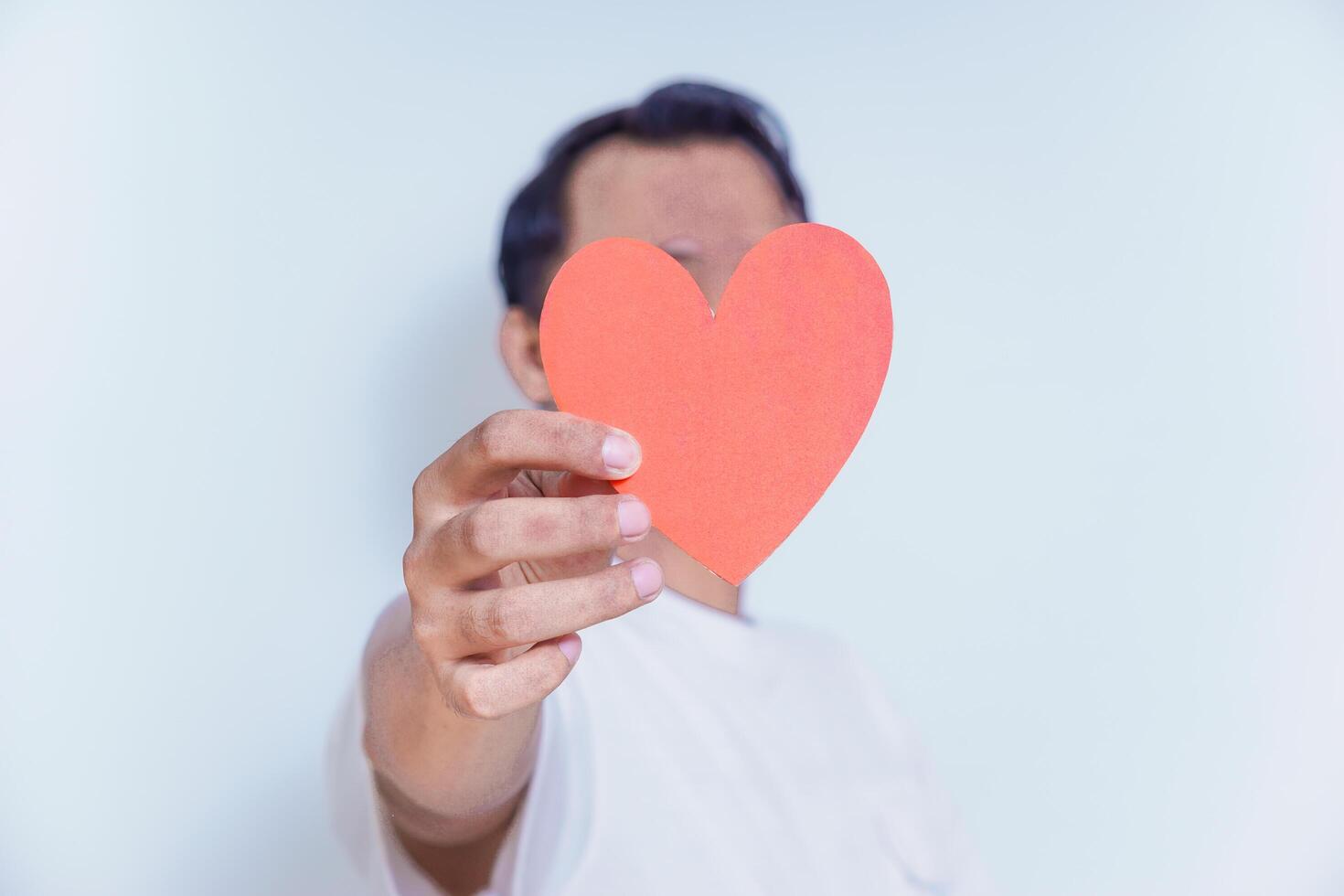 A person holds up a red heart-shaped cutout, symbolizing love and affection against a clean white background. World Heart Day concept photo