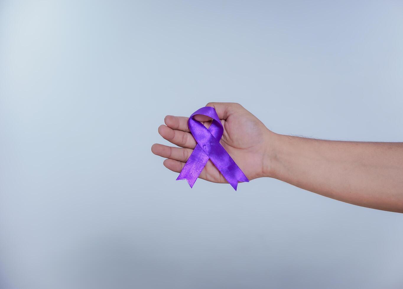 A hand holds a purple ribbon, symbolizing awareness and support for various causes, including domestic violence and cancer. Healthcare and World cancer day concept photo