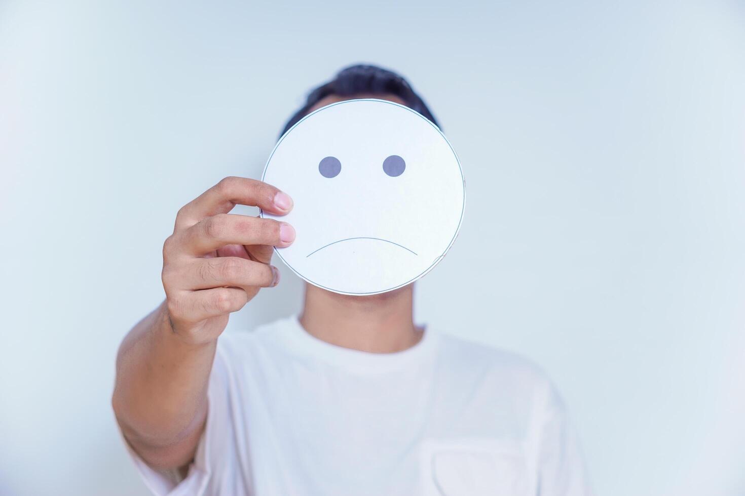 A person holds a sad face symbol, reflecting emotions and the complexity of feelings we often hide. world mental health day concept photo