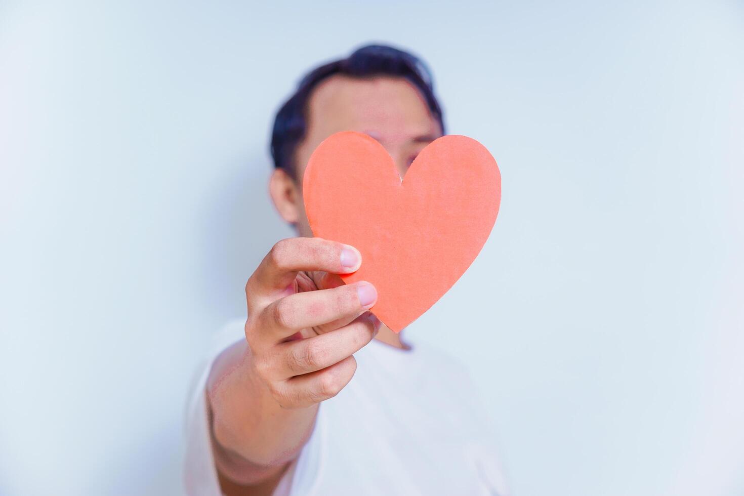 A person holds up a red heart-shaped cutout, symbolizing love and affection against a clean white background. World Heart Day concept photo