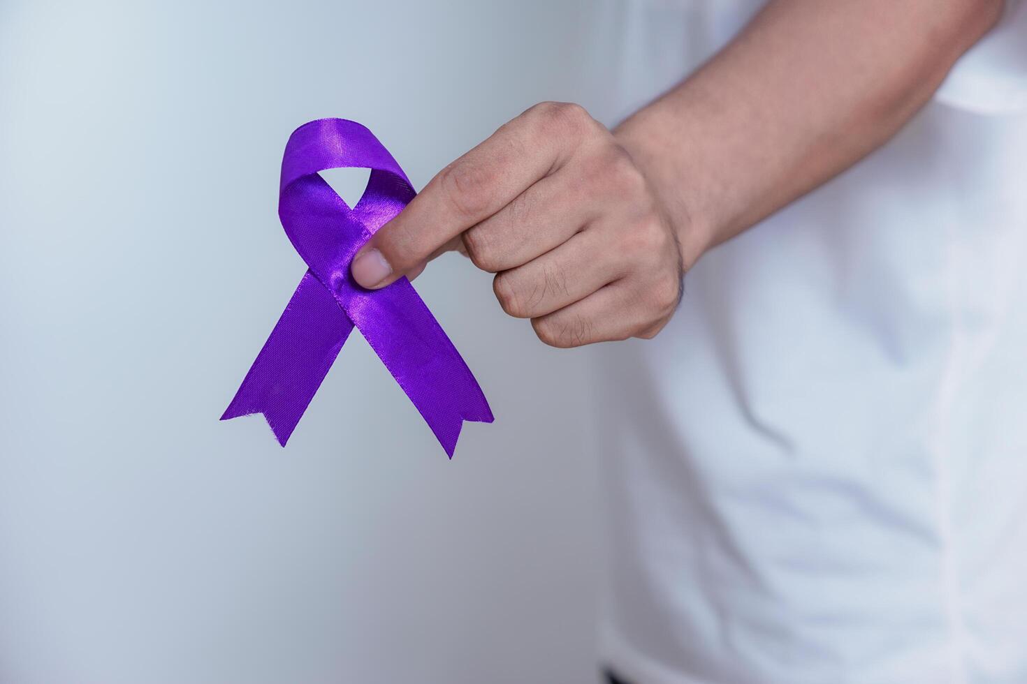 A hand holds a purple ribbon, symbolizing awareness and support for various causes, including domestic violence and cancer. Healthcare and World cancer day concept photo