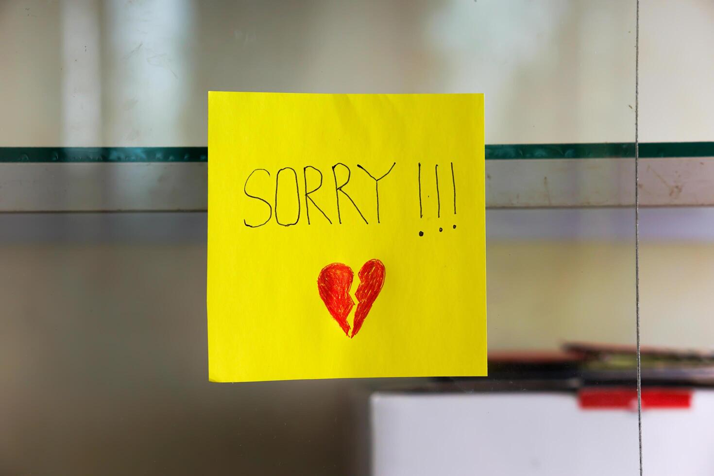 A heartfelt note on a yellow sticky note expresses deep remorse with a broken heart drawing. photo