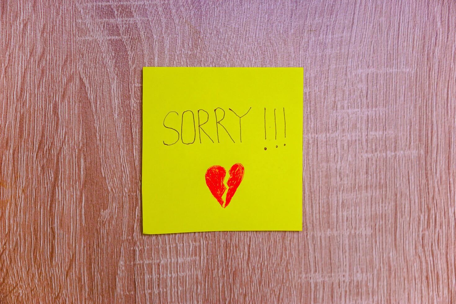 A heartfelt note on a yellow sticky note expresses deep remorse with a broken heart drawing. photo