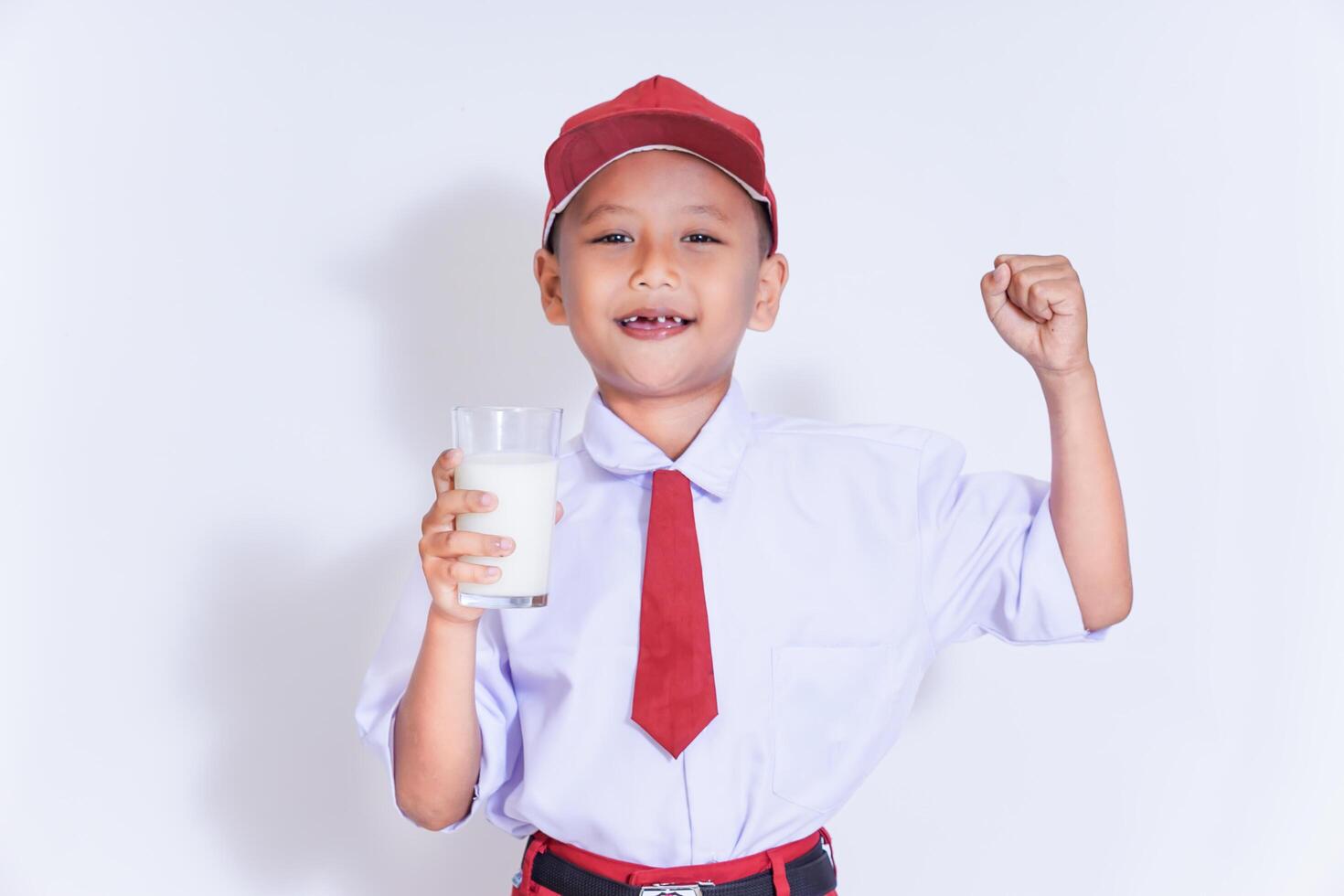 A cheerful young boy in a red uniform holds a glass of milk, showcasing confidence and joy. photo