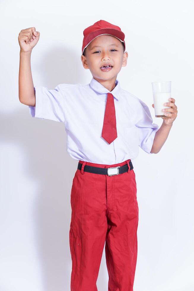 A cheerful young boy in a red uniform holds a glass of milk, showcasing confidence and joy. photo