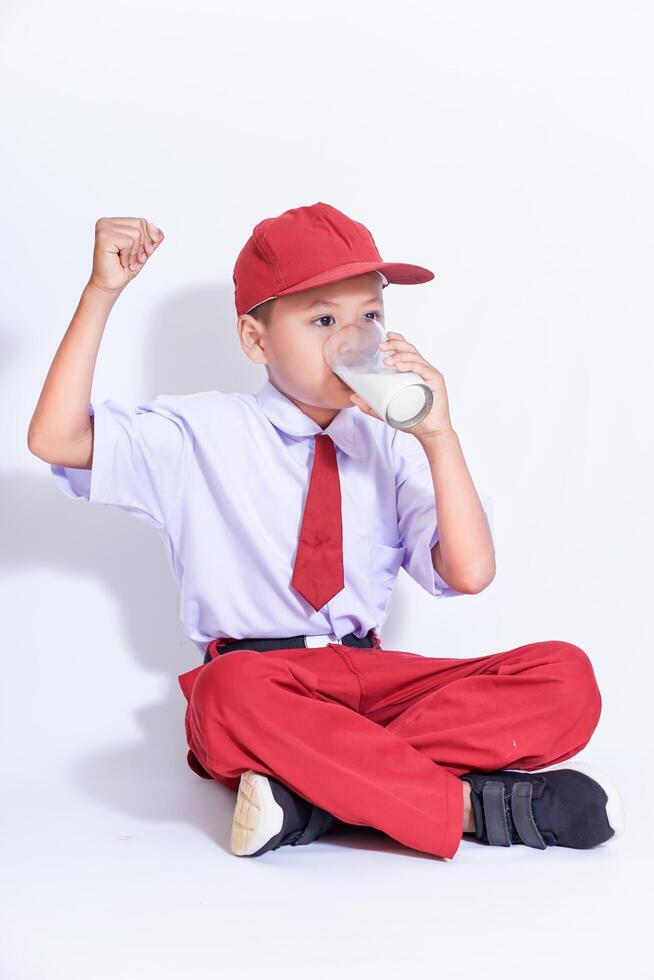 A cheerful child in a red cap and uniform outfit enjoys a glass of milk, celebrating good health and happiness. photo