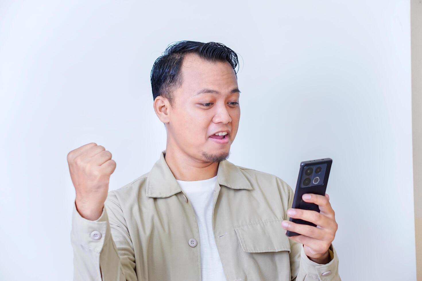 A surprised man expressing excitement and shock while hold smartphone and raised hands. photo