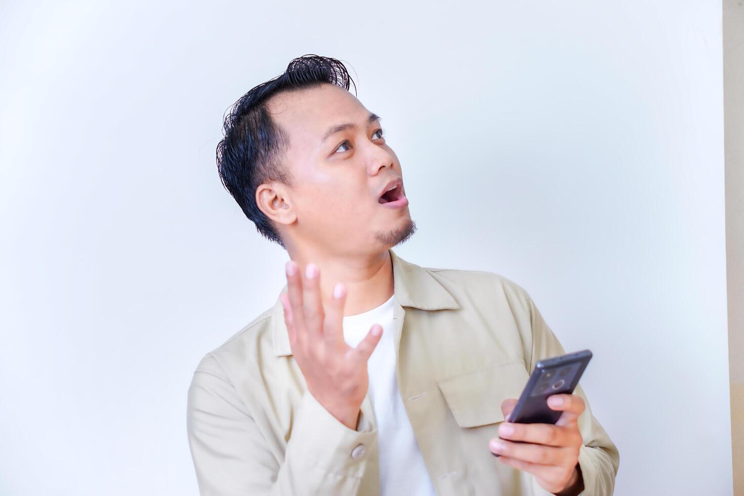A surprised man gestures while holding his smartphone, expressing surprise or confusion. photo