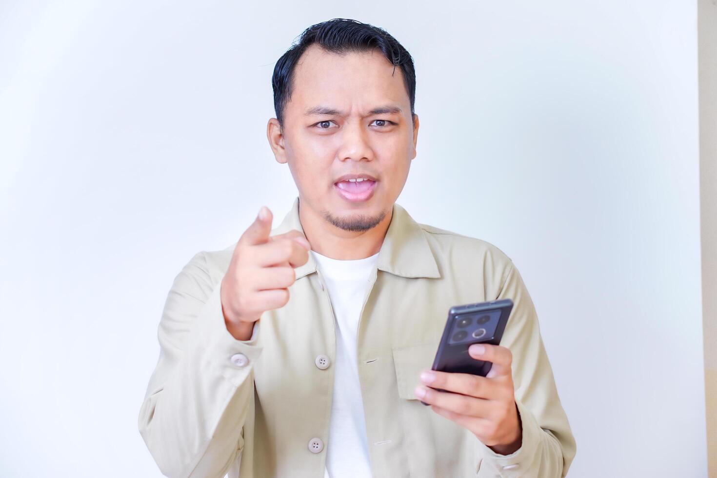 Confident man pointing while holding a phone, conveying strong emotions and engagement photo