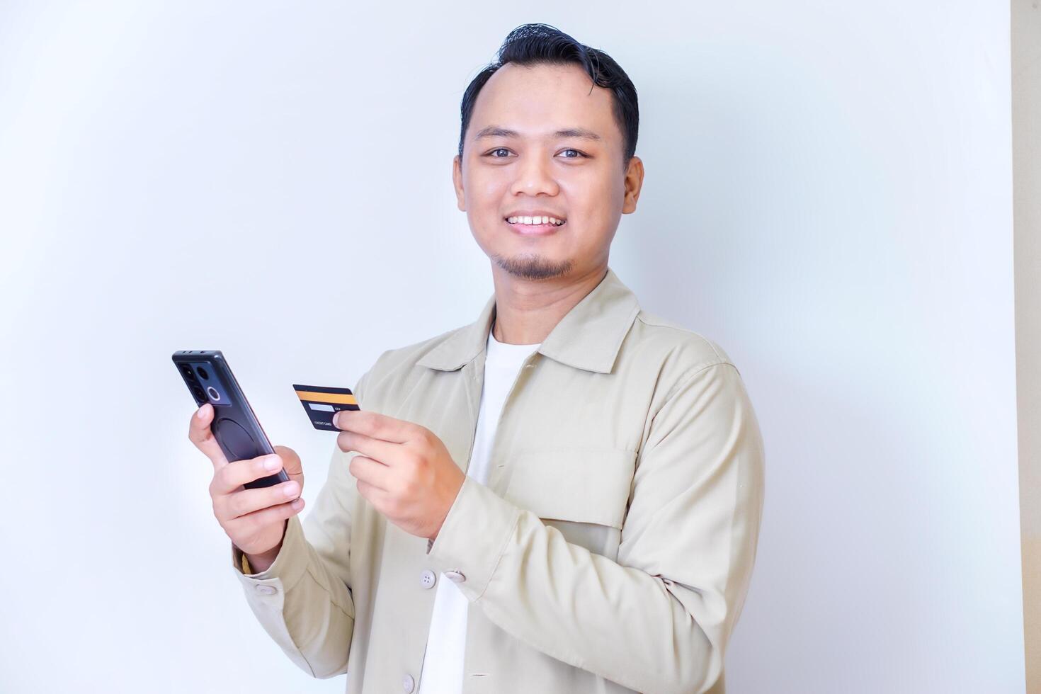 A cheerful man holding a smartphone and credit card, ready for a transaction. photo