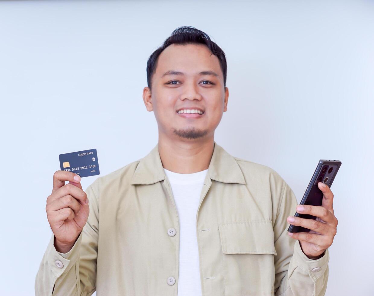 A cheerful man holding a smartphone and credit card, ready for a transaction. photo