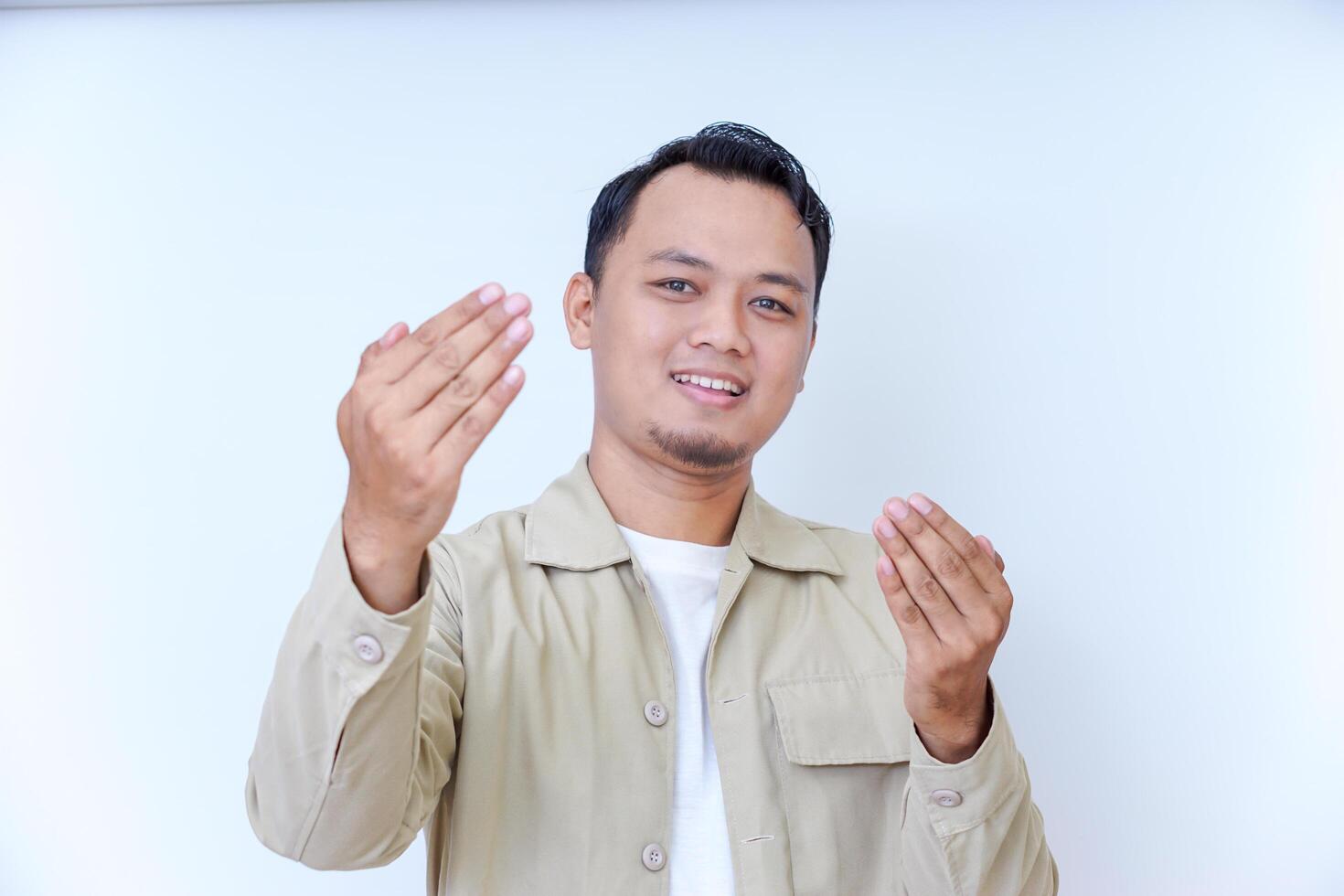 A smiling man with an inviting gesture, wearing a beige jacket against a light background. photo