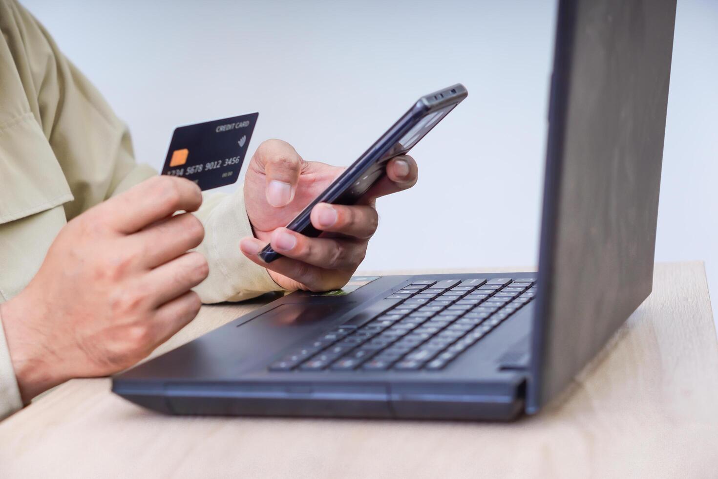 A person using a smartphone and credit card for online transactions at a laptop. photo